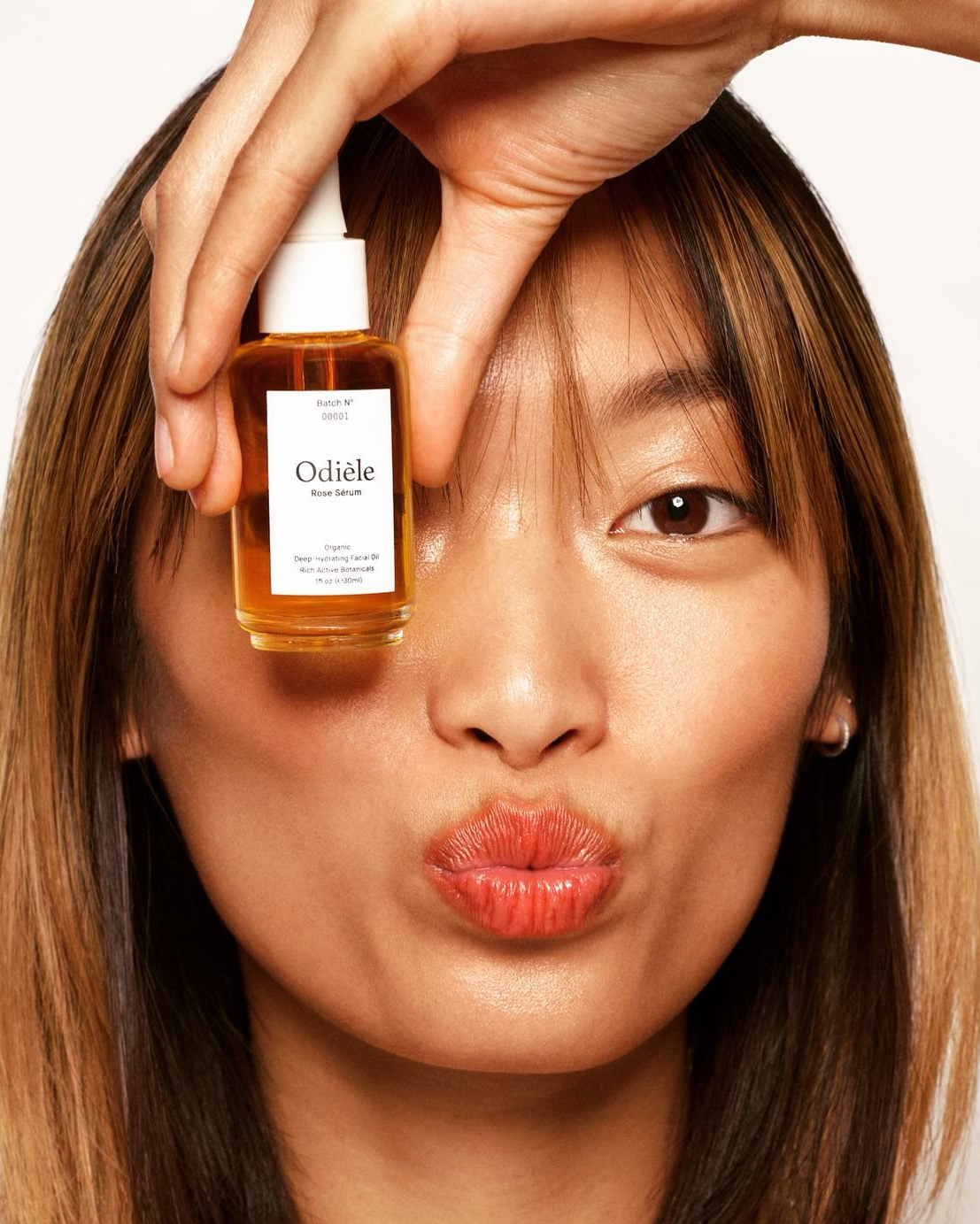 Person holding a bottle of Oliie skincare product in front of their face on a white background